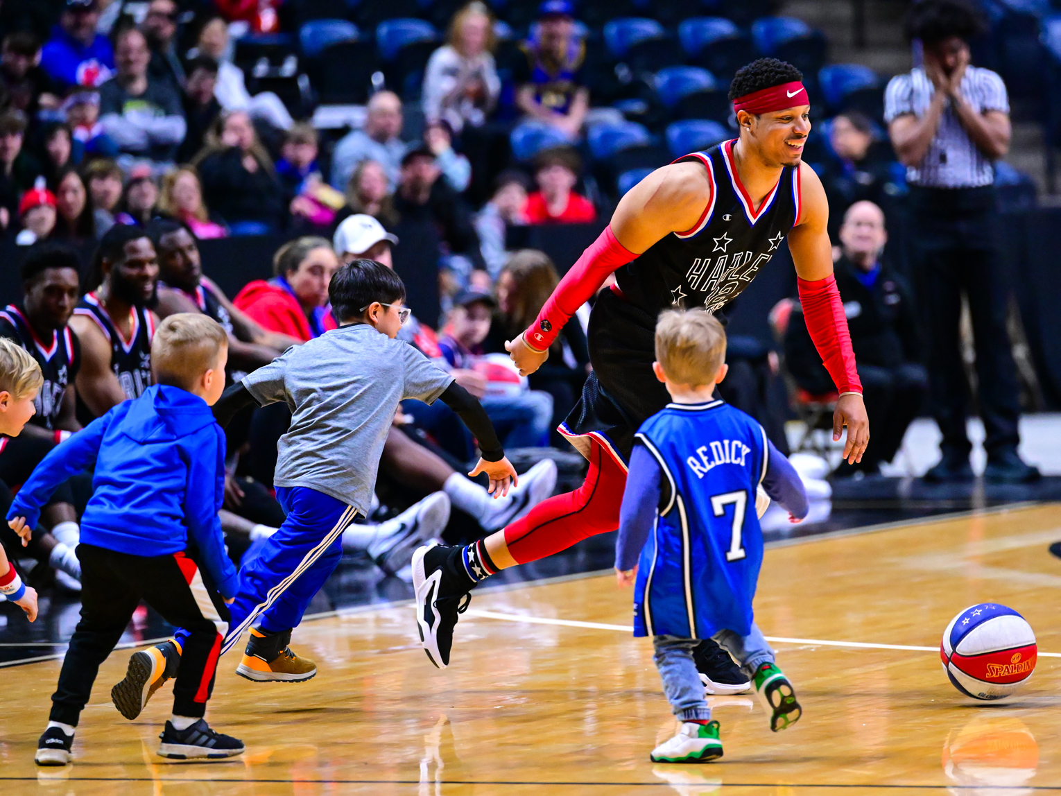 Das Foto zeigt einen männlichen Spieler der Harlem Globetrotters, wie er gegen vier kleine Jungs Basketball spielt.