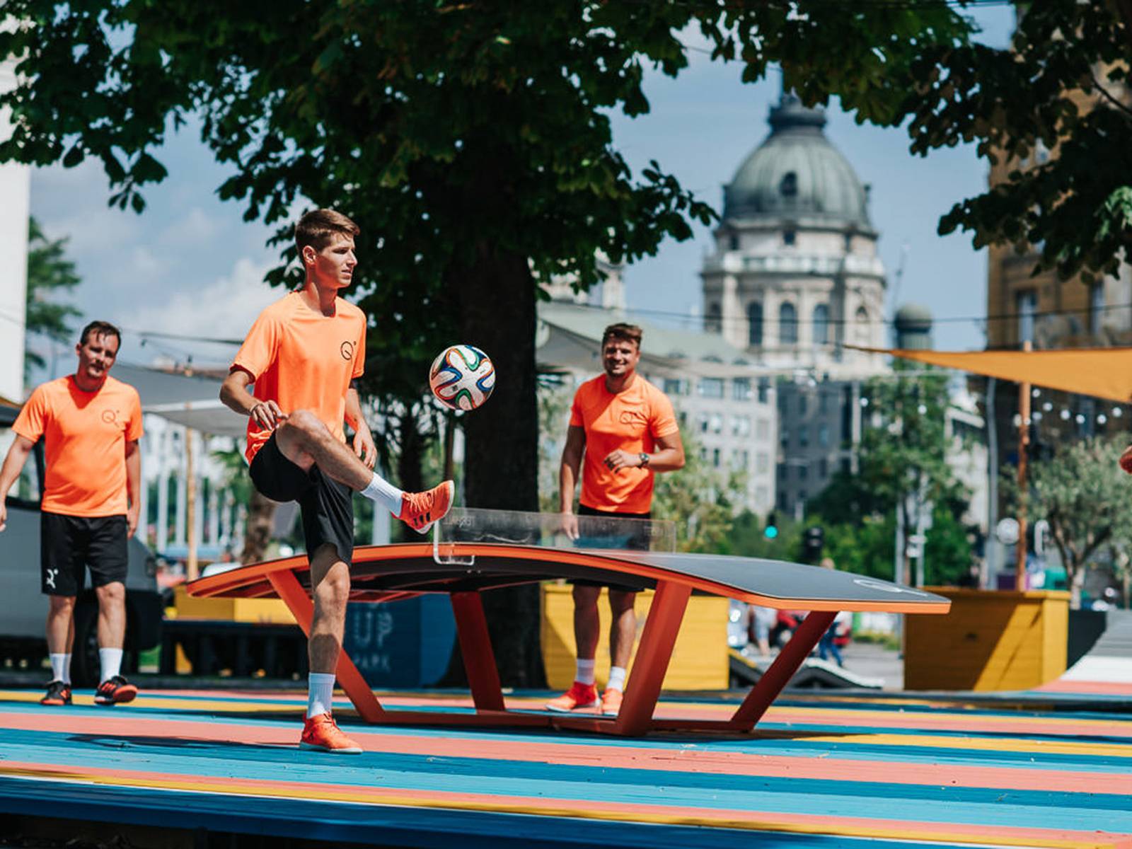 Drei Personen mit einem Ball. Sie stehen um eine gewölbte Tischtennisplatte.