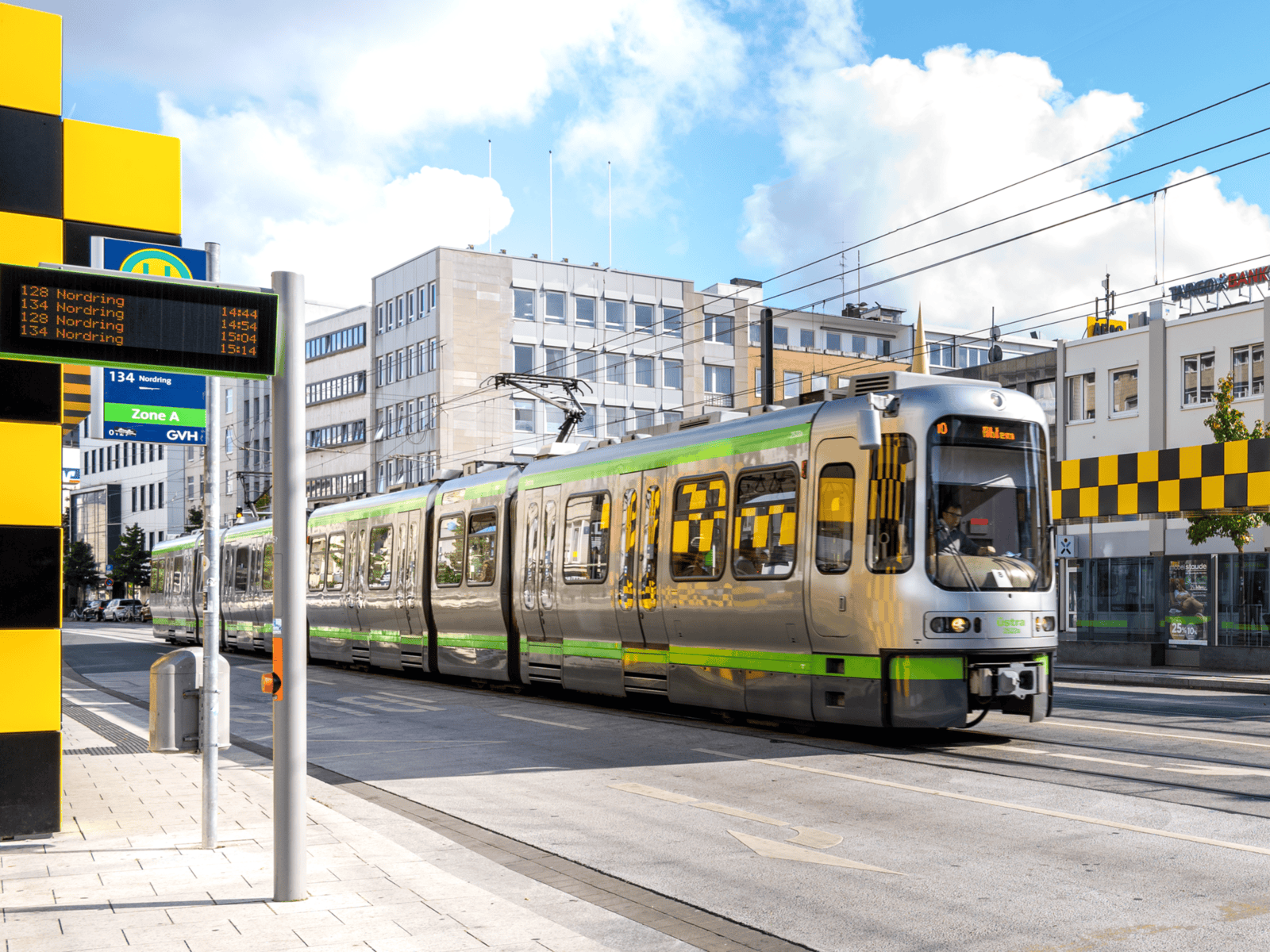 Straße, eine Haltstelle und eine Stadtbahn, dahinter Gebäude