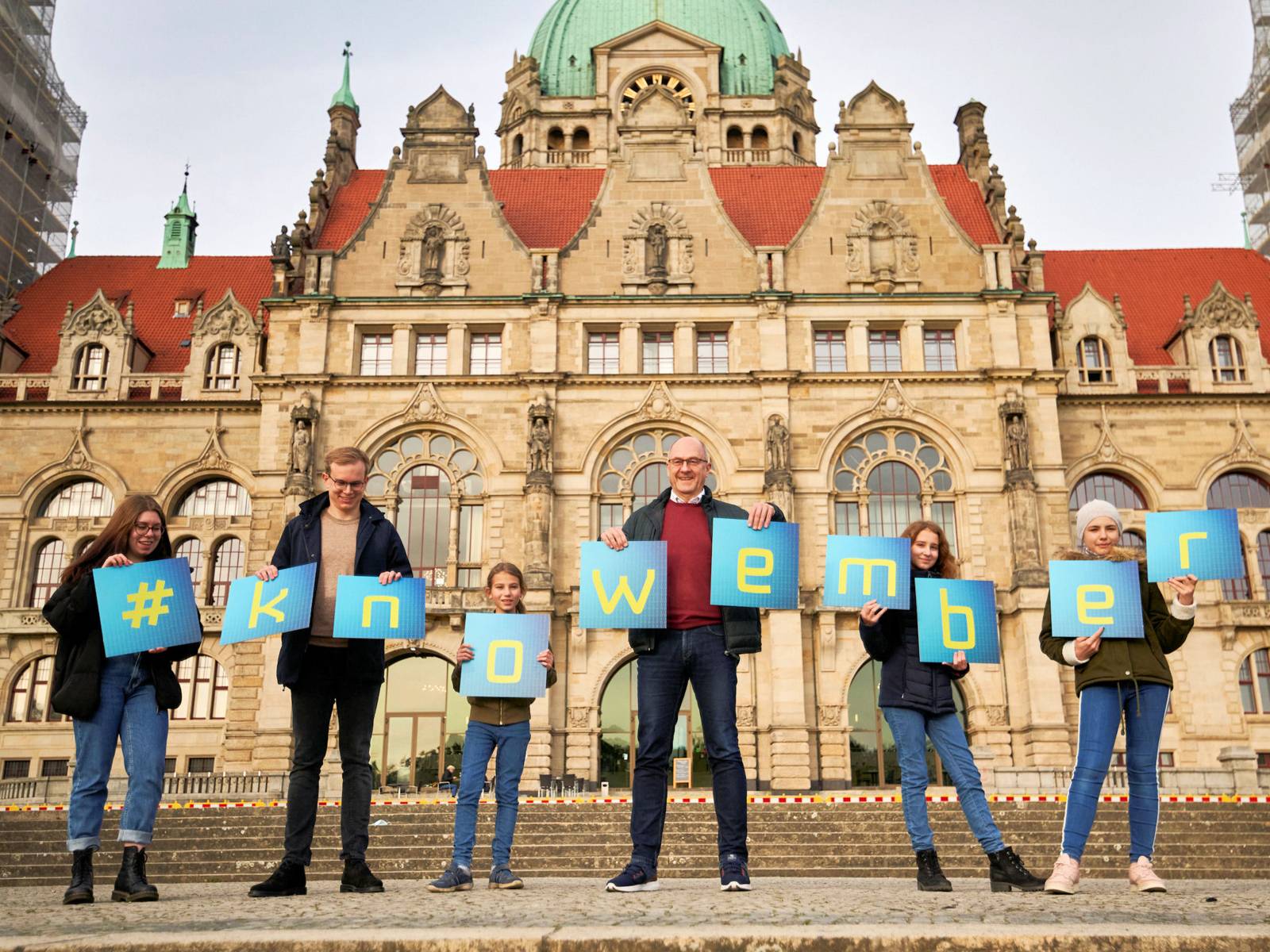 Menschen stehen vor einem historischen Gebäude und halten Tafeln in den Händen, die den Begriff #knowember bilden.