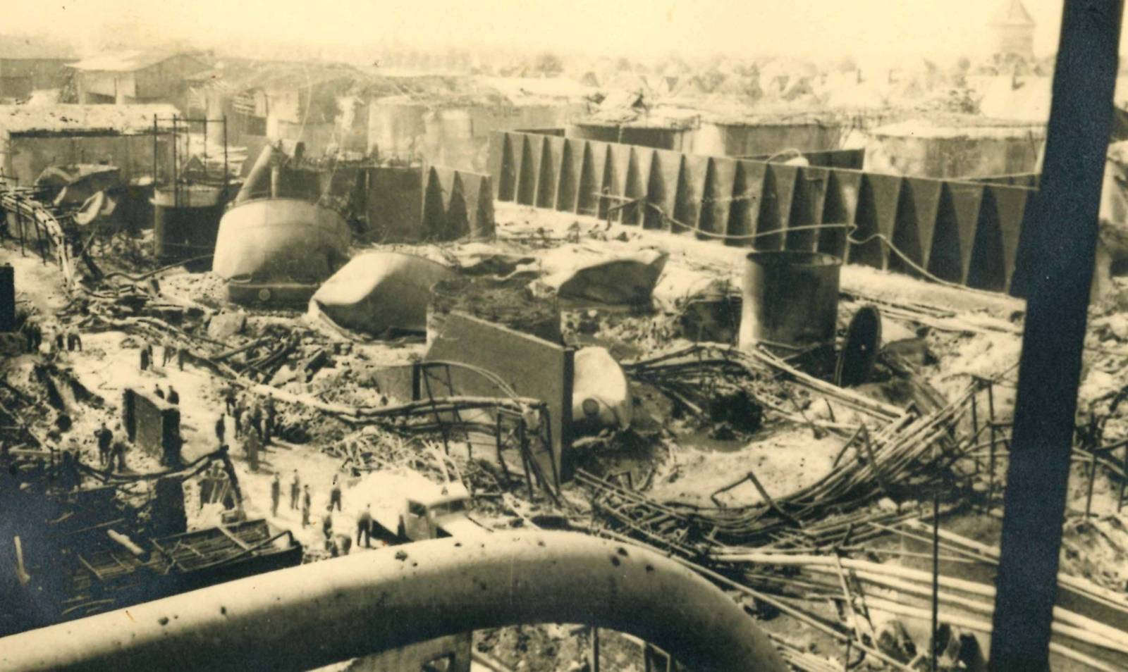 Trümmer einer Tankgruppe nach einem Luftangriff, Sommer 1944. Im Vordergrund Militärs und Zivilpersonen, rechts im Hintergrund der Misburger Wasserturm.