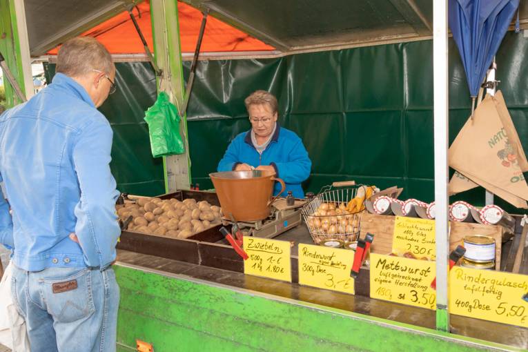 Ein Kunde kauft auf dem Wochenmarkt Misburg Kartoffeln und Wurstwaren.