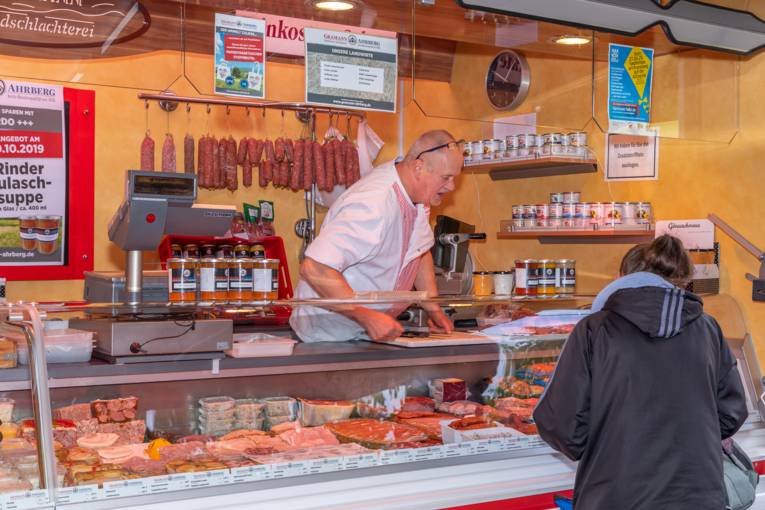 Ein Verkäufer bietet einer Kundin seine Wurst- und Fleischwaren an.