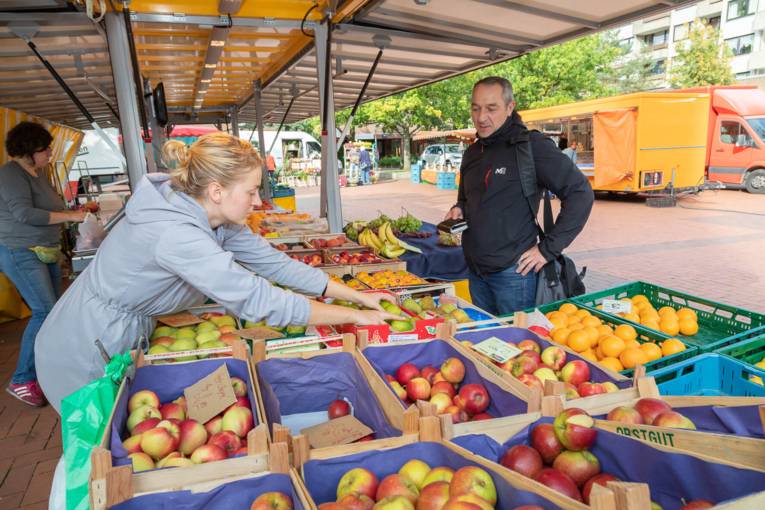 Ein Kunde kauft bei einer Obsthändlerin auf dem Wochenmarkt ein.