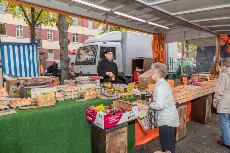 Eine Kundin kauft Eier und Honig bei einem Verkäufer auf dem Wochenmarkt.