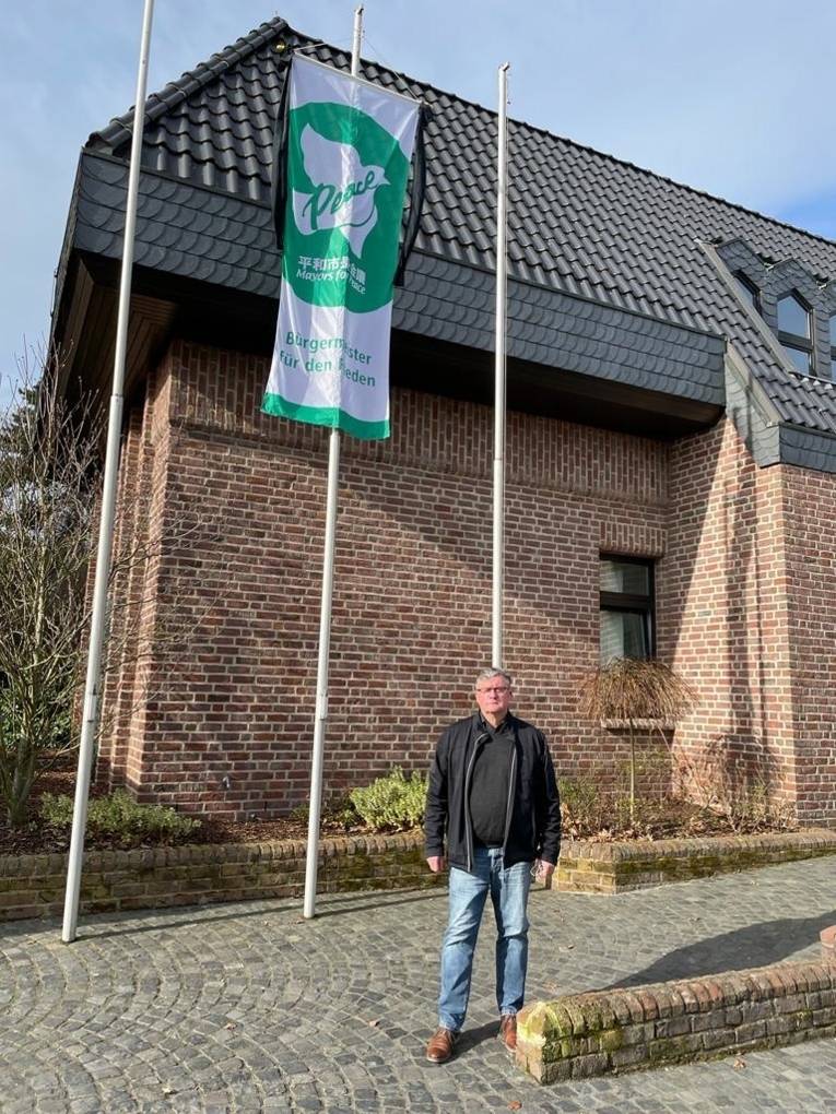 Ein Mann steht vor der Mayors for Peace-Flagge