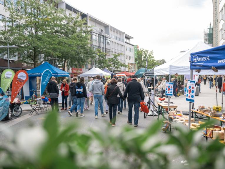 Eine Gruppe Menschen geht auf einer Straße. An den Seiten stehen verschiedene Pavillons.