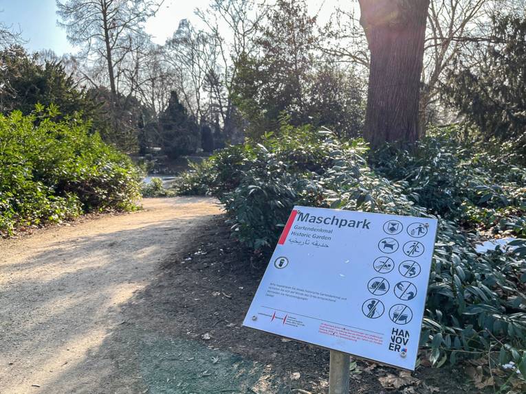 Blick in einen Park. Am Rand steht ein Schild, auf dem "Maschpark" steht.