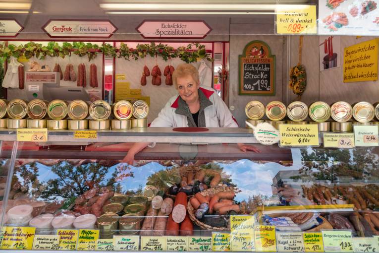 Eine Verkäuferin steht in ihrem Verkaufswagen für Wurstwaren.