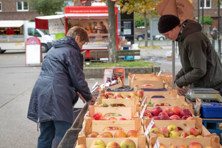 Eine Kundin und ein Verkäufer an einem Stand, an dem frische Äpfel verkauft werden.